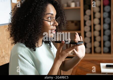 Giovane donna afroamericana che dettava messaggio vocale al cliente, chattando con un amico, registrando audio Foto Stock