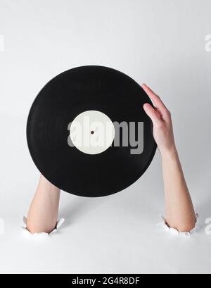 Le mani femminili ruotano un disco in vinile attraverso i fori strappati di uno sfondo bianco. Arte creativa stile retro Foto Stock