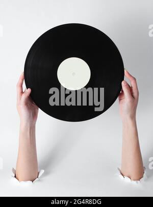 Mani femminili che tengono un disco di vinile attraverso i fori strappati di sfondo bianco. Arte creativa stile retro Foto Stock