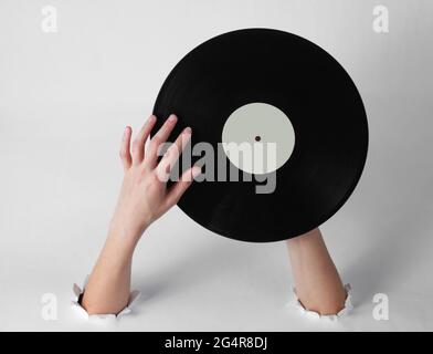 Le mani femminili ruotano un disco in vinile attraverso i fori strappati di uno sfondo bianco. Arte creativa stile retro Foto Stock