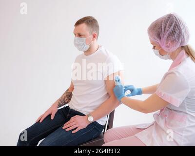medico che tiene la siringa e che usa il cotone prima di fare l'iniezione a paziente maschile in una maschera medica. Vaccino Covid-19 o coronavirus Foto Stock