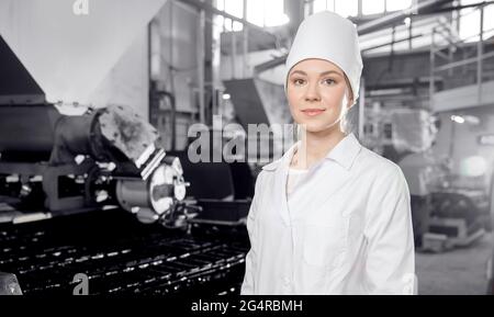 Baker donna che tiene il pane fresco in mani su sfondo automatico fabbrica di panetteria. Concetto industriale alimentare moderno. Foto Stock