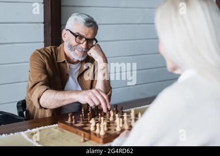 Uomo anziano sorridente che gioca a scacchi con moglie in primo piano sfocato Foto Stock