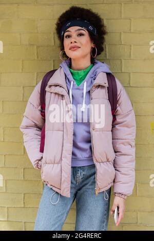 Donna afroamericana di stile in piedi vicino al muro giallo di mattoni Foto Stock