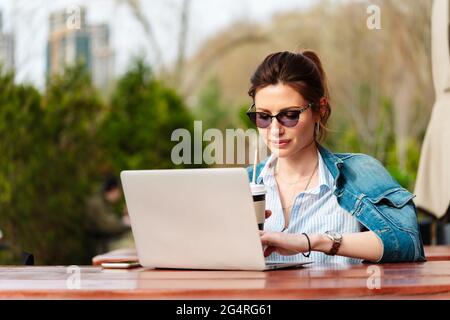 Giovane donna che lavora a un computer portatile in un bar su una veranda esterna Foto Stock