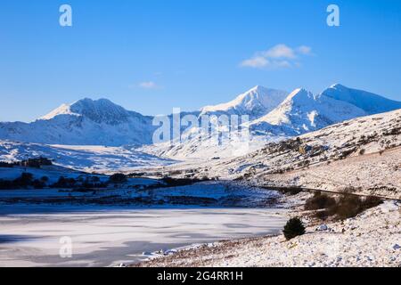 Vista attraverso i laghi ghiacciati di Llynnau Mymbyr fino al ferro di cavallo di Snowdon nel Parco Nazionale di Snowdonia con neve profonda in inverno. Capel Curig Galles del Nord Gran Bretagna Foto Stock