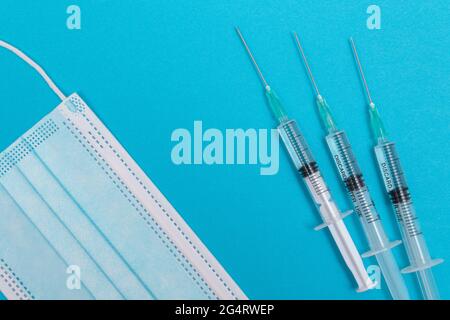 Diverse siringhe e maschere facciali sul tavolo blu - Vista dall'alto. Le siringhe sono preparate per la vaccinazione o l'iniezione. Esperimento medico. Maschera medica monouso blu. Protezione da virus - Flat Lay Foto Stock