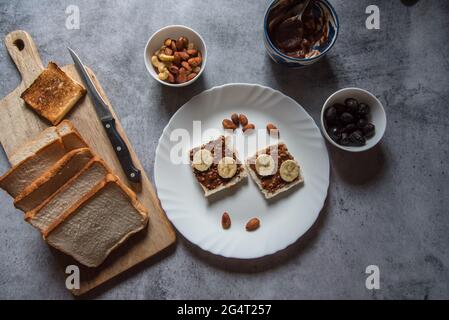 Ingredienti salutari per la colazione pane, burro di arachidi, banane, mandorle, noci, latte di frutta asciutto. Concetto di cibo sano e sano. Foto Stock