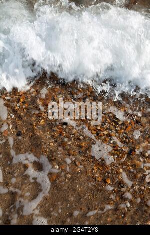 Primo piano di piccole onde che si infrangono sulla spiaggia, creando bolle e schiuma Foto Stock