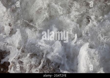 Primo piano di piccole onde che si infrangono sulla spiaggia, creando bolle e schiuma Foto Stock