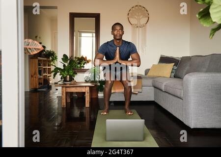 Uomo africano in posa sedia durante una lezione di yoga online Foto Stock