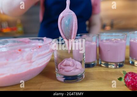 il processo di preparazione di un dessert alla fragola dal latte. Cuoco mette il pudding in tazze e decora Foto Stock