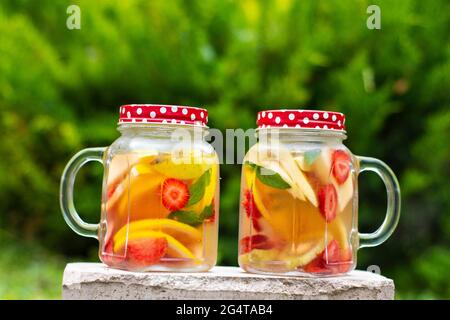Due vasetti di vetro, deliziosa bevanda detox con frutti rossi, arancioni e gialli, in piedi sulla pietra. Occhiali con messa a fuoco selettiva. Foto Stock