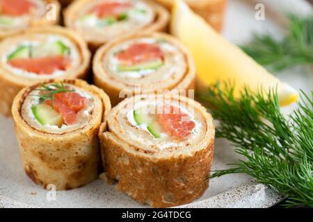 Panini crespati di salmone con cetriolo e formaggio cremoso su un piatto, vista closeup. Antipasto gourmet Foto Stock