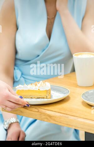 La mano della cameriera mette il pezzo di cupcake sul tavolo in un caffè, la mano della donna sta mettendo un po 'di pasta rotonda sul tavolo su uno sfondo di una femmina in un vestito blu Foto Stock