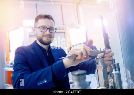 Il tecnico controlla le dimensioni con calibro a corsoio al dettaglio della finitura dopo la lavorazione dei metalli su macchine utensili cnc. Qualità di controllo concettuale del prodotto Foto Stock