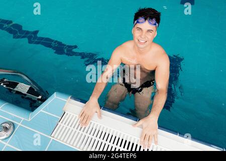 Nuotatore giovane che indossa occhiali di formazione in piscina blu acqua. Foto Stock