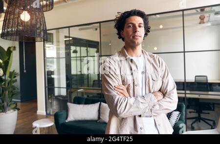 Ritratto di giovane uomo casualmente vestito in piedi in un moderno ufficio open space della sua nuova attività Foto Stock