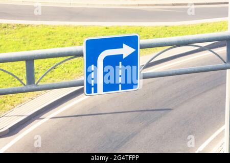 Cartello blu con una freccia che gira dalla corsia esterna sullo sfondo di un'uscita autostradale Foto Stock