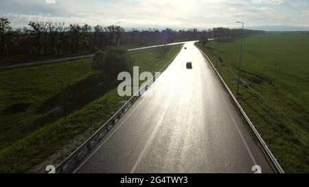 Drone sopra strada asfaltata bagnata per auto tra campi seminato Foto Stock