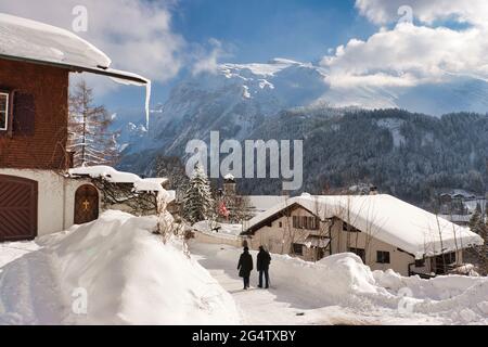 Una scena invernale di case, chalet e tetti ricoperti da uno spesso strato di neve, anche una passeggiata di coppia a Engelberg, Cantone di Obvaldo, Svizzera centrale Foto Stock