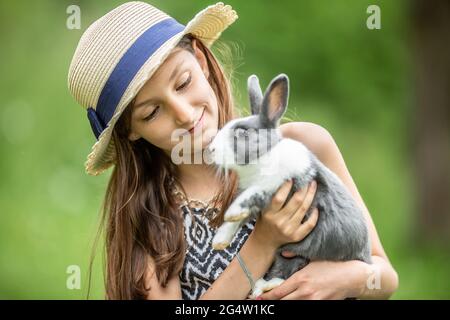 Bambino giovane che tiene felicemente un coniglio grigio nelle mani e che gioca con esso. Foto Stock