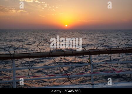 Tramonto sull'Oceano Indiano da poppa di una nave con la ringhiera ferita con filo di rasoio in caso di attacco da parte di pirati o terroristi per smettere di salire a bordo Foto Stock