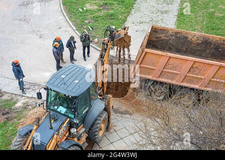BIELORUSSIA, MINSK - 17 MAGGIO 2021: Un trattore con una benna escavatore scava un foro e carica sabbia nella parte posteriore di un dumper. Fotografia di scorta. Foto Stock