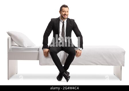 Foto a lunghezza intera di un uomo d'affari in un vestito e cravatta seduta su un letto isolato su sfondo bianco Foto Stock