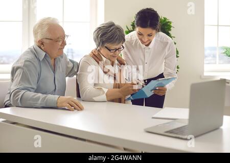 Coppia senior firmano un contratto legale in ufficio durante un incontro con un consulente finanziario. Foto Stock