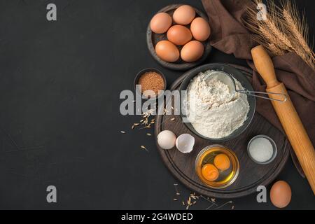 Un set di ingredienti per cucinare piatti dall'impasto alla cottura. Uova e farina su fondo nero. Foto Stock