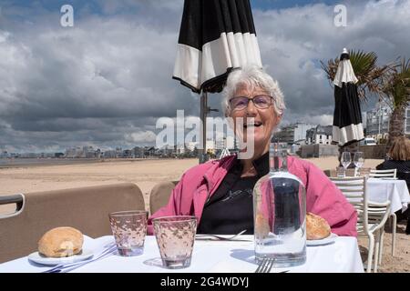 Una donna anziana seduta a un tavolo da ristorante su una spiaggia in Bretagna Foto Stock