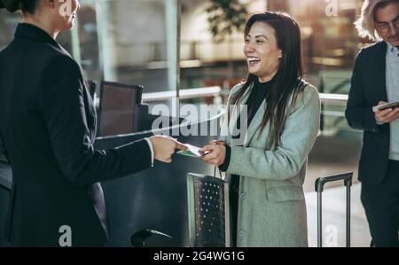 Donna sorridente che mostra la sua carta d'imbarco e il passaporto all'assistente di volo al terminal dell'aeroporto. Donna d'affari che effettua il check-in del volo all'aeroporto. Foto Stock