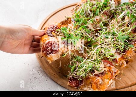 Pezzo di pinsa romana in mano con mozzarella stretching con salame, formaggio, funghi, decorato con micrograni su tavola di legno Foto Stock