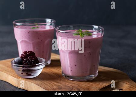 Frullati fatti in casa con bacche nere surgelate in due vetri trasparenti su tavola di legno su sfondo grigio scuro. Primo piano Foto Stock