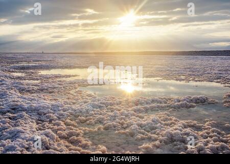 Spiaggia cristallina di sale bianco illuminata dal sole del mattino riflessa in piccole piscine con acqua di mare al Mar Morto - il lago più ipersalino del mondo Foto Stock