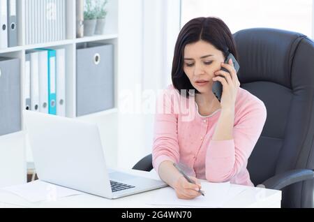 Bella donna di affari che parla al telefono e prendere appunti Foto Stock