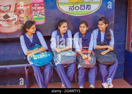 Quattro studentesse indiane che indossano uniformi blu si siedono in attesa alla fermata dell'autobus, Udupi, Karnataka, India Foto Stock