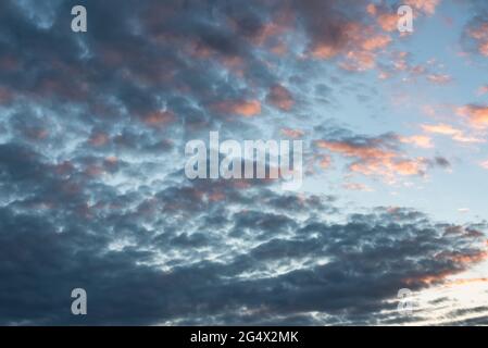 foto del cielo tormentoso y tranquilo con nubes cumulus estractus azules, blancas, naranjas y negra , con un molino de agua de fondo, orizzontale Foto Stock