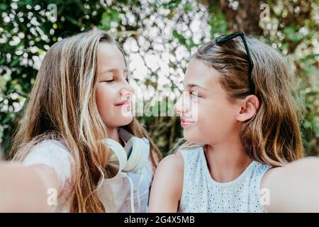 Sorridi le ragazze che si guardano l'un l'altro mentre prendono selfie in giardino Foto Stock