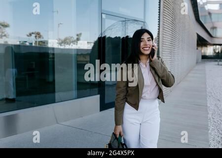Professionista femminile con borsa che parla sul telefono cellulare Foto Stock