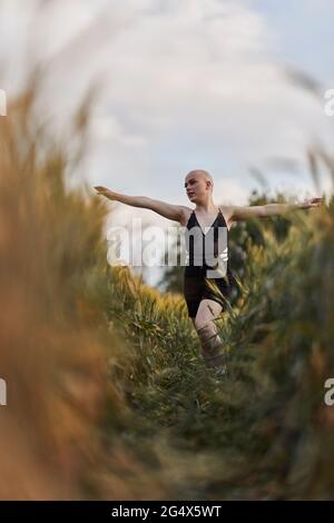 Donna calva transgender in abito nero che cammina con le braccia allungate in campo agricolo Foto Stock