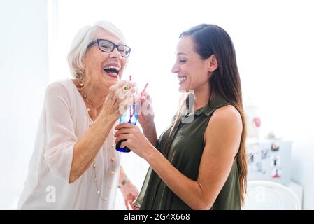 Donna anziana allegra con nipote che condivide un bicchiere di succo mentre si trova in cucina Foto Stock