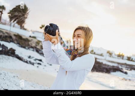 Giovane donna sorridente che fotografa attraverso la macchina fotografica in spiaggia Foto Stock