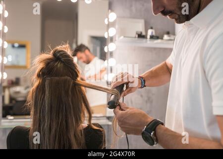 Parrucchiere maschile con piastra per capelli su capelli del cliente femminile presso il salone Foto Stock