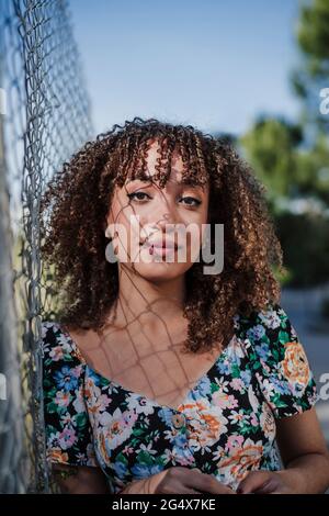 Bella giovane donna con capelli ricci appoggiati su recinzione Foto Stock