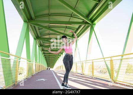 Sorridente giovane donna che fa segno di pace mentre si sta in piedi sul ponte Foto Stock