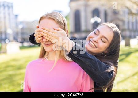 Donna sorridente che chiude gli occhi di una femmina amica al parco Foto Stock