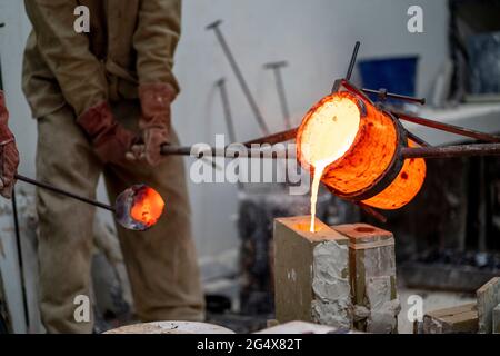 Operai che versano il bronzo fuso in un contenitore alla fonderia Foto Stock