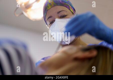 Dentista femminile che indossa una maschera protettiva per il viso che esamina i denti del paziente in clinica Foto Stock